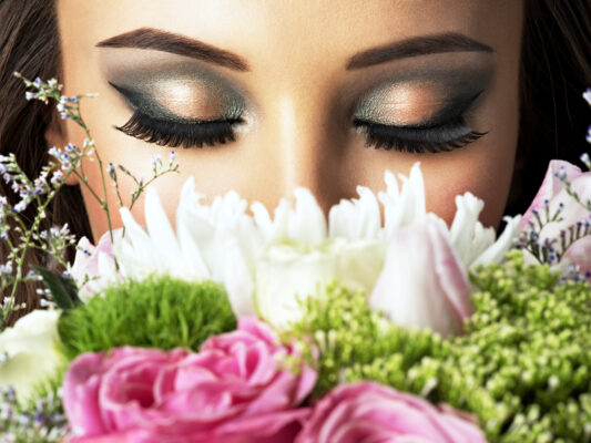 Closeup face by falsies/ false eyelash of beautiful girl with flowers. Young attractive woman holds the bouquet of spring flowers. LavisLash US