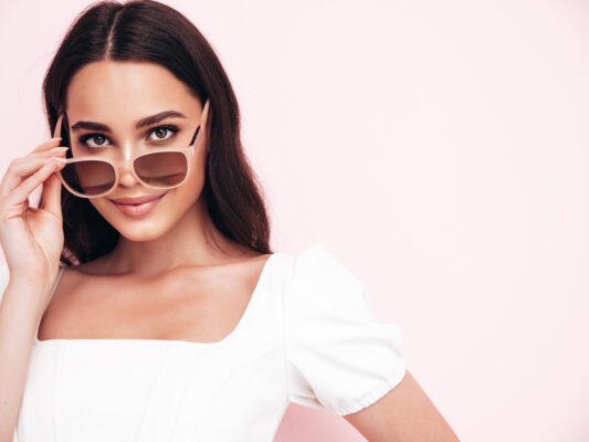 fashion-beauty-portrait-young-brunette-woman-with-long-curly-hair-lashes-posing-studio-pink-background-taking-off-sunglasses